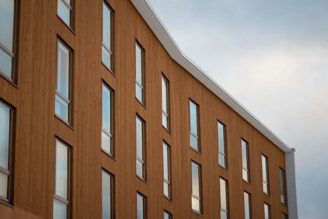 Fasada nowoczesnego budynku z pionowym drewnianym odeskowaniem, wąskie prostokątne okna i skośny dach