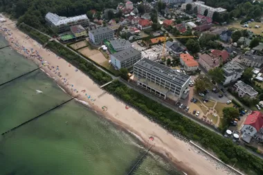 Widok z lotu ptaka na piaszczystą plażę nad morzem, z zabudową i placem budowy tuż przy brzegu.