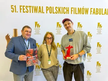 Trzy osoby pozują podczas 51. Festiwalu Polskich Filmów Fabularnych, jedna z nich trzyma program festiwalowy, a druga czerwoną statuetkę.
